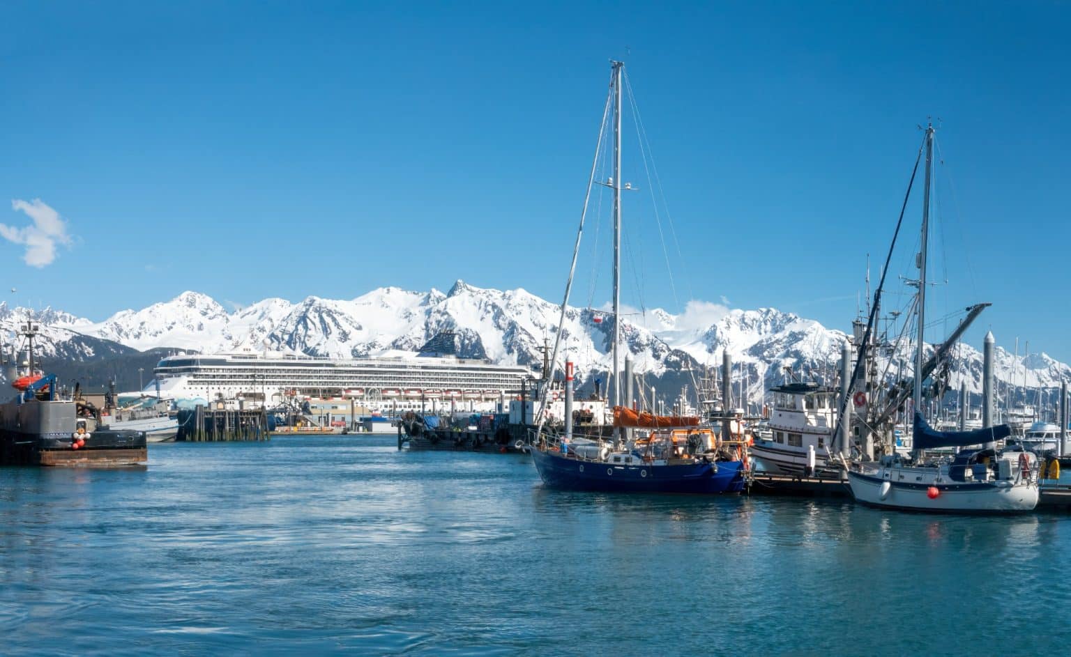 In de haven van Nome in Alaska liggen vissersboten en een cruiseschip aangemeerd, met op de achtergrond de Kenai Mountains bedekt met sneeuw.