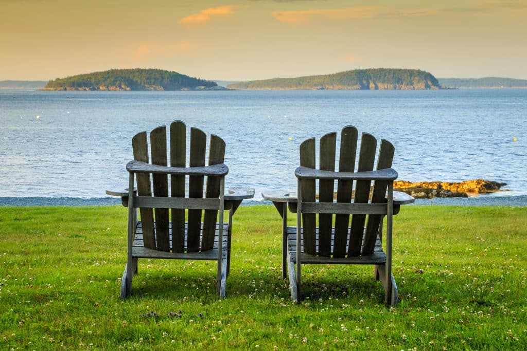Twee Adirondack stoelen op grasveld met uitzicht over zee en eilanden in Maine