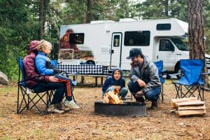 Gezin bij kampvuur naast camper op camping