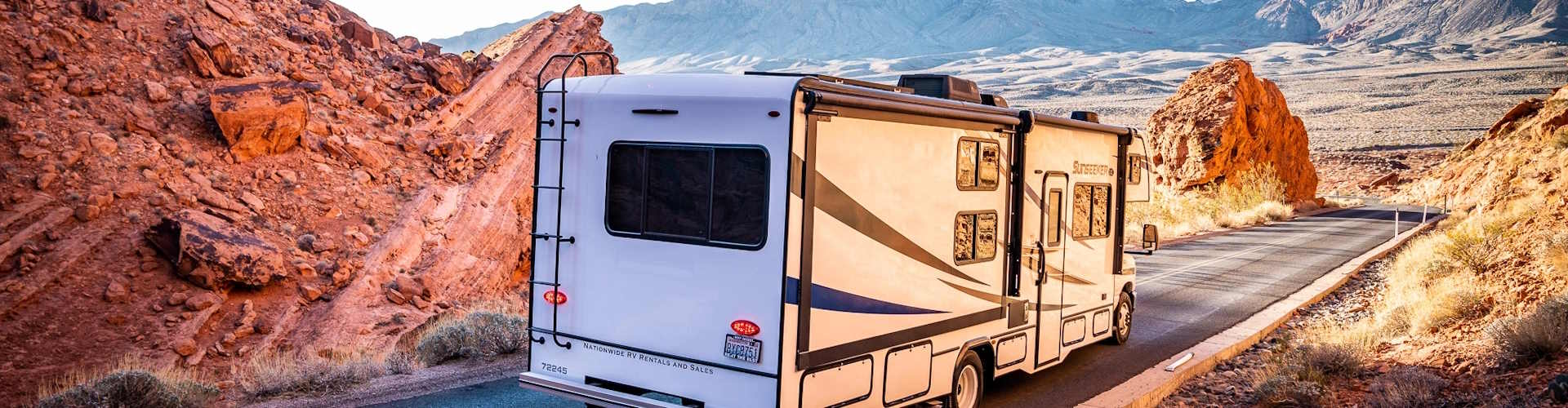 Achterzijde van de Mighty Class C Large camper op een weg in rotsachtig landschap